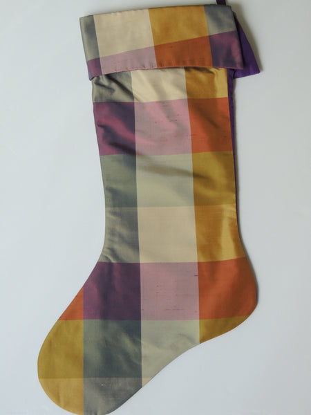 A multicolored plaid Christmas stocking with a beige, purple, and green checkered pattern and a tassel at the top.